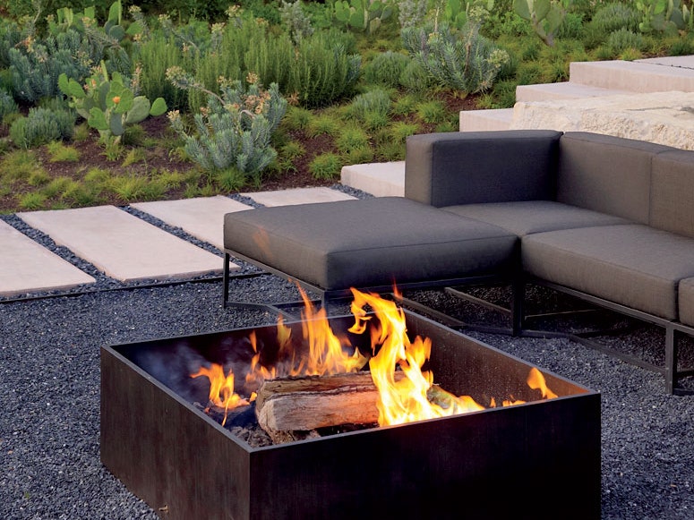 One of the best fire pits in a pebble patio with green schrubs